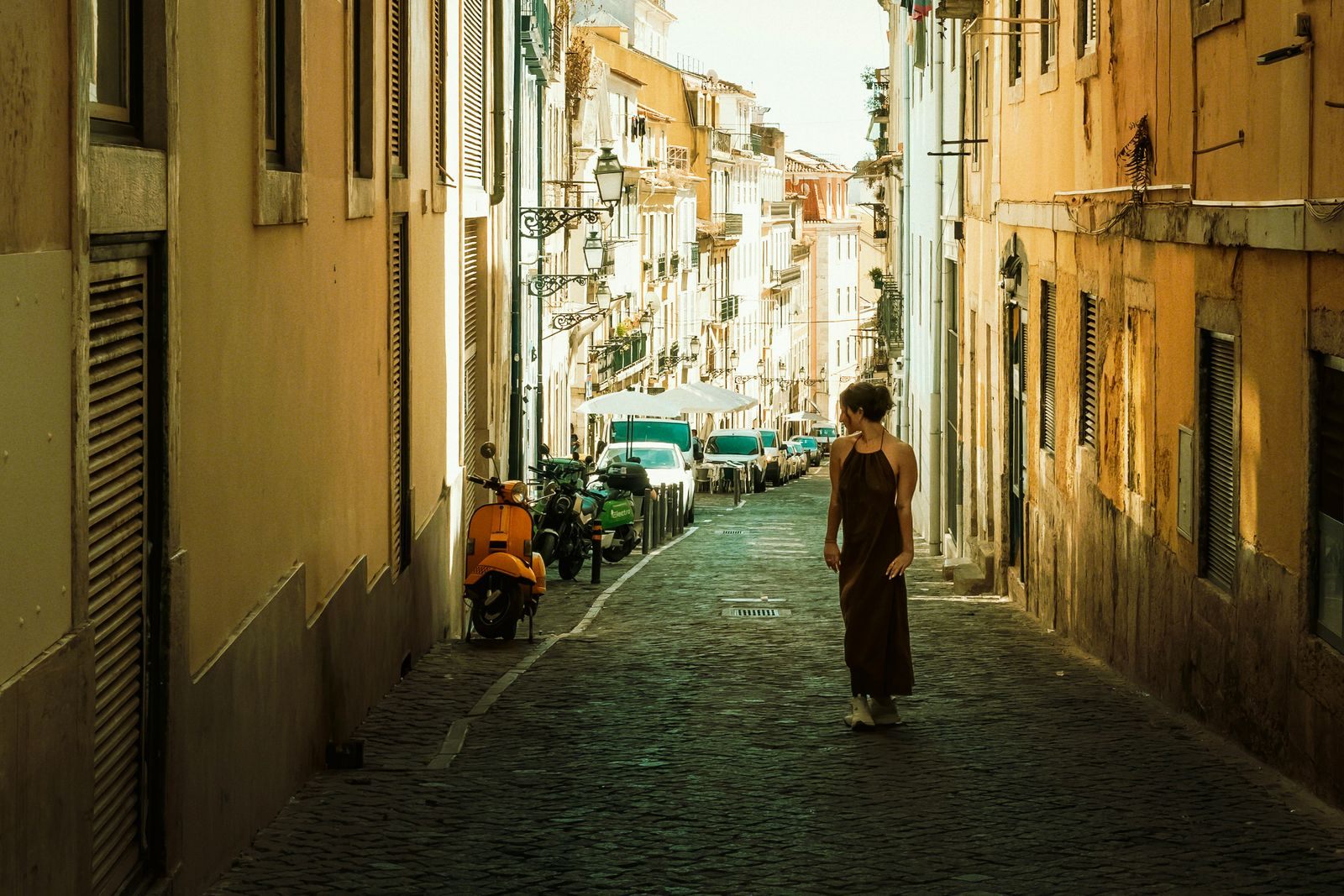 Woman walking alone down a sunlit cobbled street in Lisbon, a port of call on many solo cruise Europe itineraries