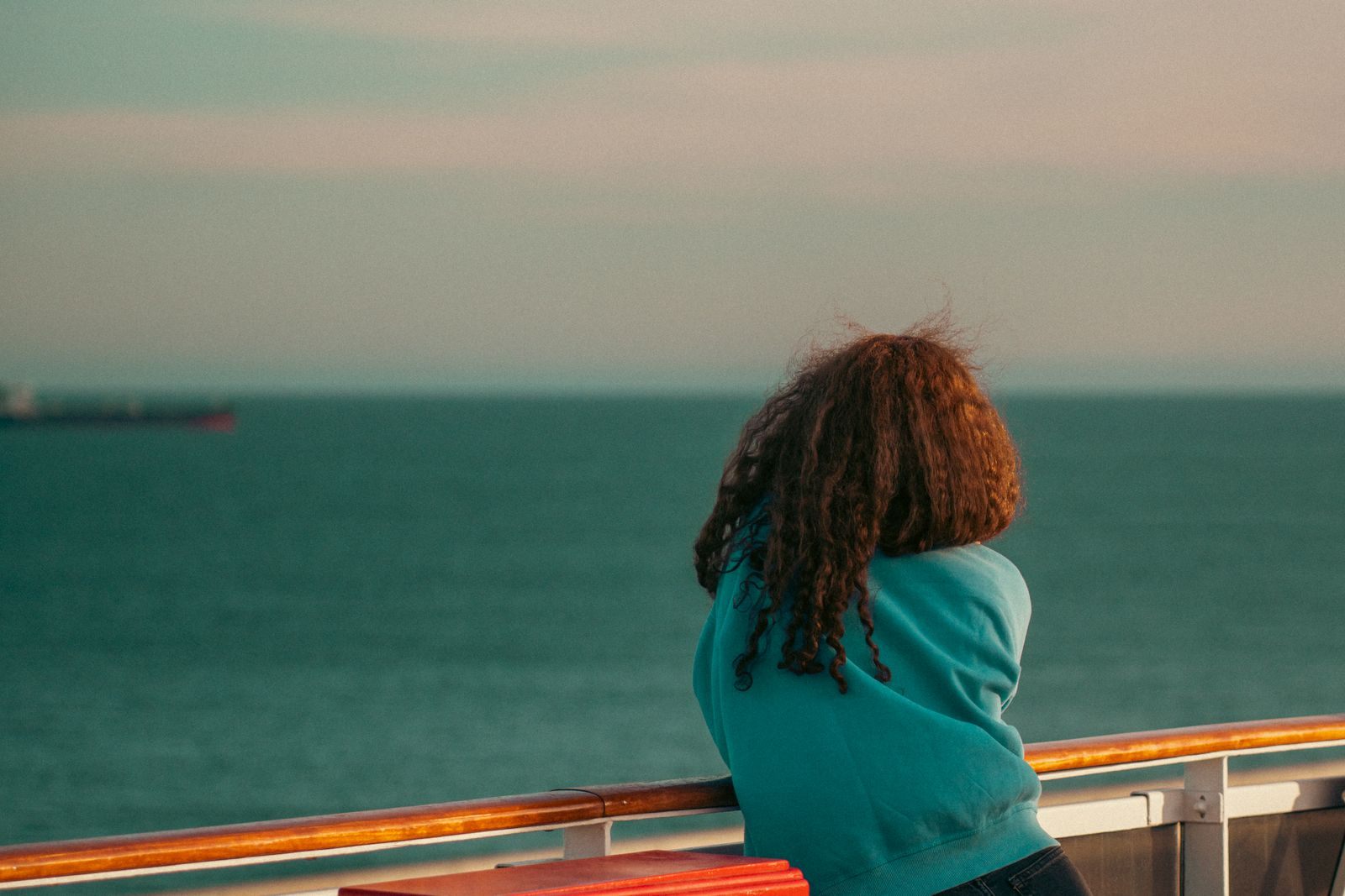 Woman traveling alone leaning on a ship rail and looking out to sea, the quiet side of solo travel cruises