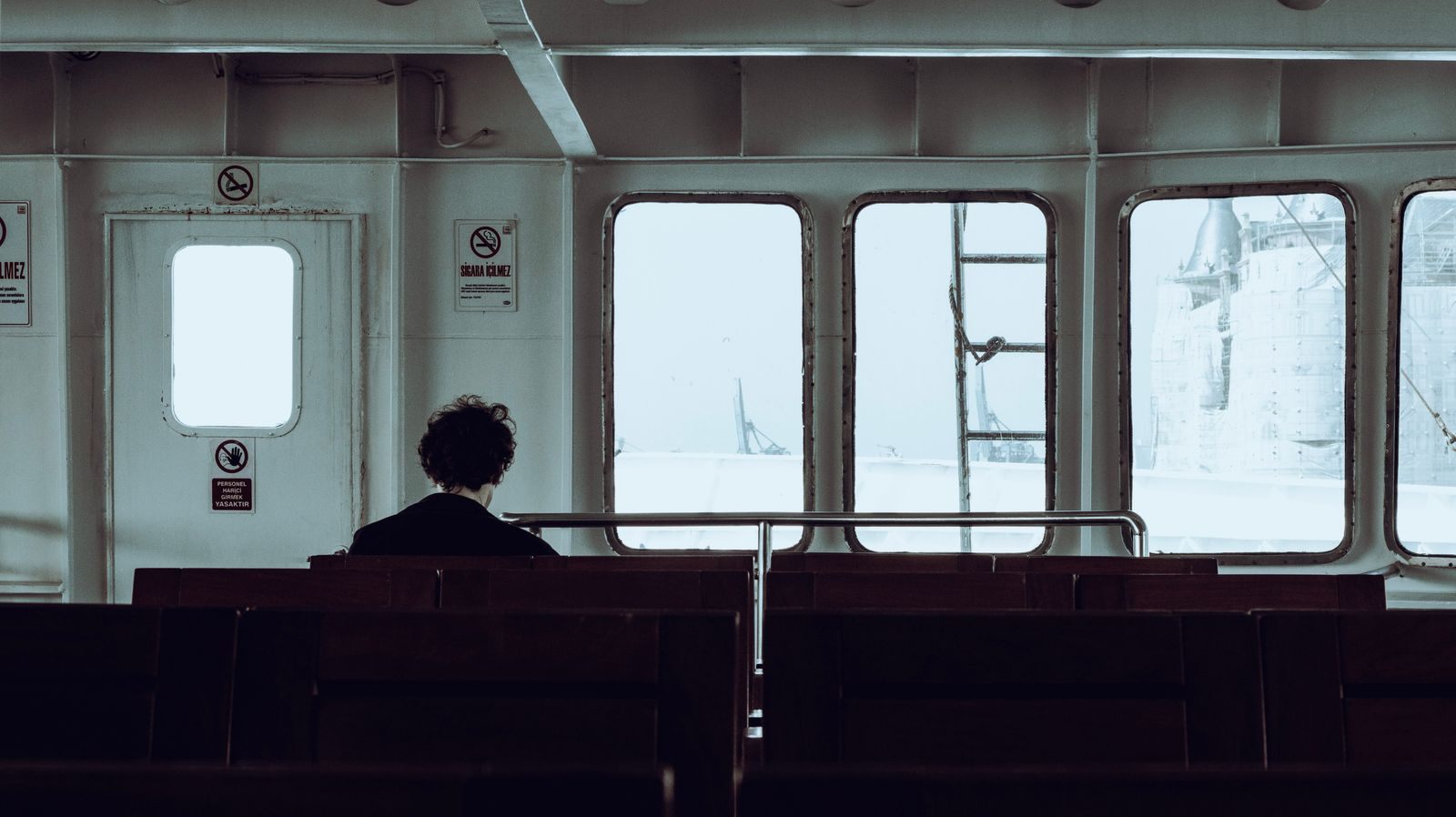 Person sitting alone in a ferry lounge looking out the windows at the sea
